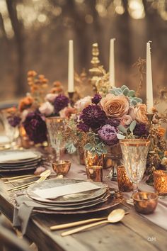 the table is set with gold and purple flowers, candles, and silverware on it