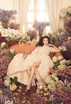 a woman in a white dress sitting on a couch surrounded by purple and white flowers