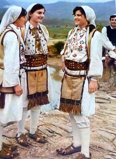 three people dressed in traditional clothing standing next to each other on a rocky area with mountains in the background