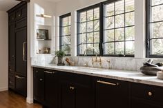 a kitchen with black cabinets and marble counter tops, gold faucets and brass pulls