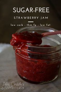 a jar filled with ketchup sitting on top of a wooden table next to a spoon