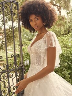 a woman in a wedding dress leaning against a gate