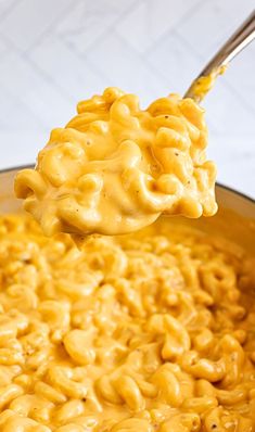 a spoon full of macaroni and cheese being lifted from a pot with it