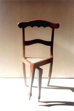 a wooden chair sitting on top of a white floor next to a wall with a shadow cast on it