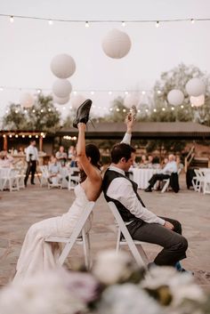 a bride and groom sitting on white chairs at their wedding reception with paper lanterns in the background