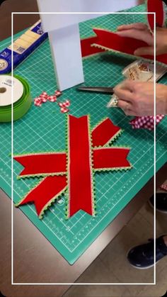 someone cutting out christmas decorations with scissors and tape on a green table top next to a pair of scissors