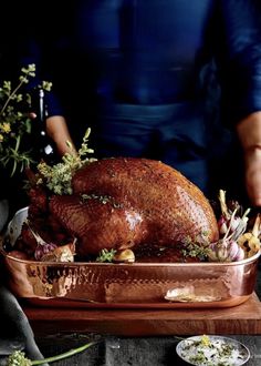 a person standing next to a roasting pan with a turkey in it and vegetables on the side