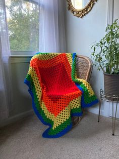 a colorful crocheted blanket sitting on top of a chair next to a potted plant