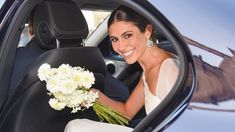 a woman sitting in the back seat of a car holding a bouquet of white flowers