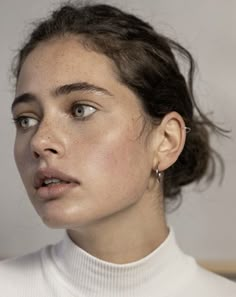 a close up of a person wearing a white shirt and silver earring on her left ear