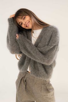 a woman in grey sweater and pants posing with her hands on her head, smiling at the camera