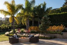 two wicker chairs sitting on top of a stone patio next to trees and bushes