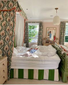 a person laying on a bed in a room with floral curtains and green dressers