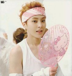 a young man holding a pink fan in his right hand and looking at the camera