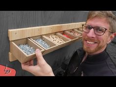 a man with glasses is holding up a wooden shelf filled with screws and nails