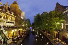 people are sitting at tables on the edge of a canal in an old european city