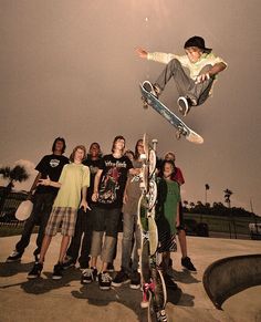 a man flying through the air while riding a skateboard next to other young people