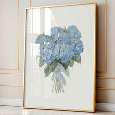 blue flowers in a gold frame on the floor next to a wall with white walls