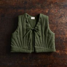 a green vest with a bow on the front and back, sitting on a wooden surface