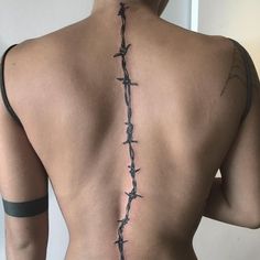 the back of a man with barbed wire on his neck and shoulder, behind him is a cross tattoo