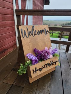 a welcome sign with flowers in it on a wooden deck next to a red barn