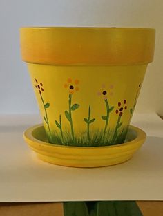 a yellow flower pot sitting on top of a white table next to a green planter