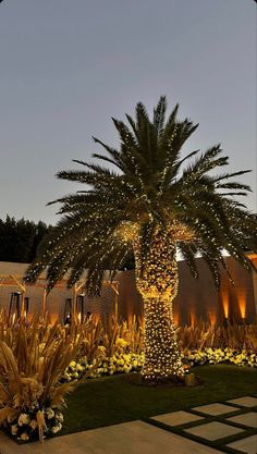 a palm tree is lit up with lights in the night sky and surrounded by flowers