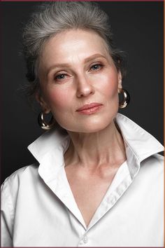 an older woman with grey hair wearing large hoop earrings and a white button up shirt