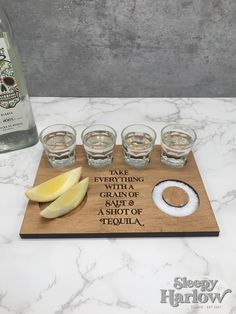 a wooden cutting board topped with glasses and lemon slices next to a bottle of booze