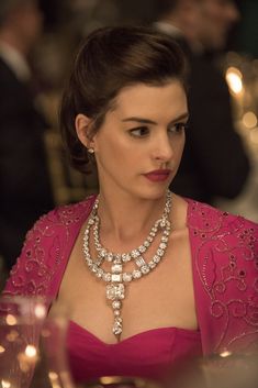 a woman in a red dress wearing a diamond necklace and tiara sitting at a table