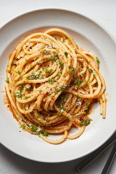 a white plate topped with pasta covered in sauce and parsley next to chopsticks