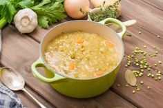 a green pot filled with soup sitting on top of a wooden table next to vegetables