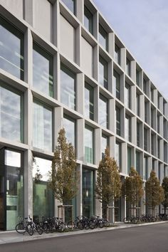 several bicycles are parked in front of a building that has many windows and trees on the side