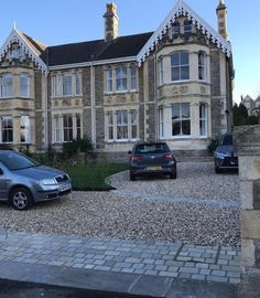 two cars are parked in front of a large house with stone driveways and cobblestones