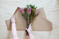 two people holding flowers on top of a piece of paper with one person reaching for it