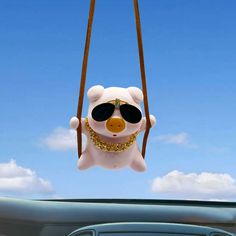 a teddy bear with sunglasses hanging from a car's front window in the air