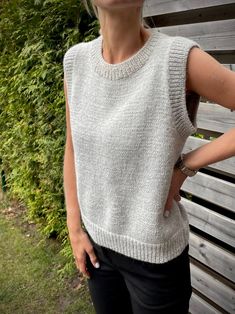 a woman standing next to a wooden bench with her hands on her hips, wearing a white sweater and black pants