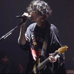 a young man holding a guitar and singing into a microphone while standing in front of an audience