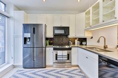 a kitchen with white cabinets and stainless steel appliances, along with a checkered rug on the floor