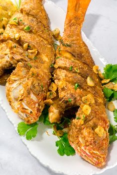 two pieces of fish on a white plate with garnishes