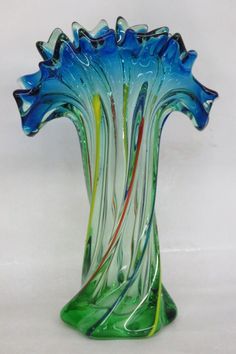 a blue and green glass vase sitting on top of a white table next to a wall