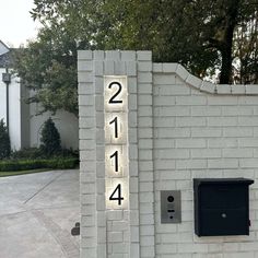 a white brick wall with numbers on it and a mailbox next to it in front of a house