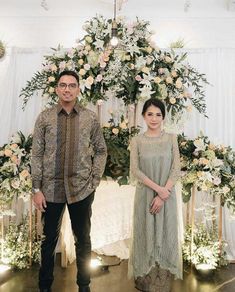 two people standing next to each other in front of a floral arch with white and pink flowers