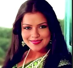 a woman with long black hair and green dress smiling at the camera, wearing earrings