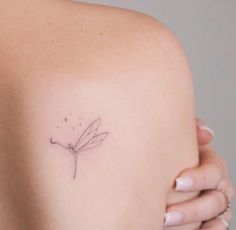 the back of a woman's shoulder with a small dragonfly tattoo on it