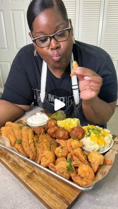 a woman sitting at a table in front of a tray of food with fried chicken