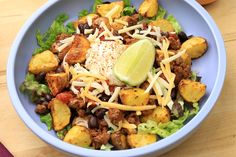 a blue bowl filled with lettuce, cheese and other food on top of a wooden table