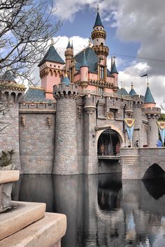 a castle with turrets and towers is reflected in the water at disneyland's magic kingdom