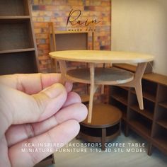 a hand holding a miniature coffee table in front of a brick wall with shelves and shelving