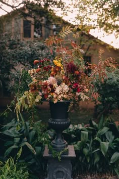 a vase filled with lots of flowers sitting on top of a metal pole in the middle of some plants